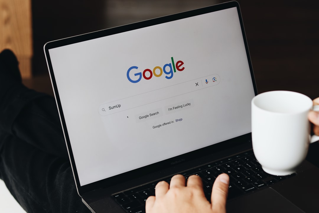 A person is using a laptop to search for SumUp on Google while holding a white coffee mug. The Google search page is displayed on the screen, and the user is preparing to click Google Search.